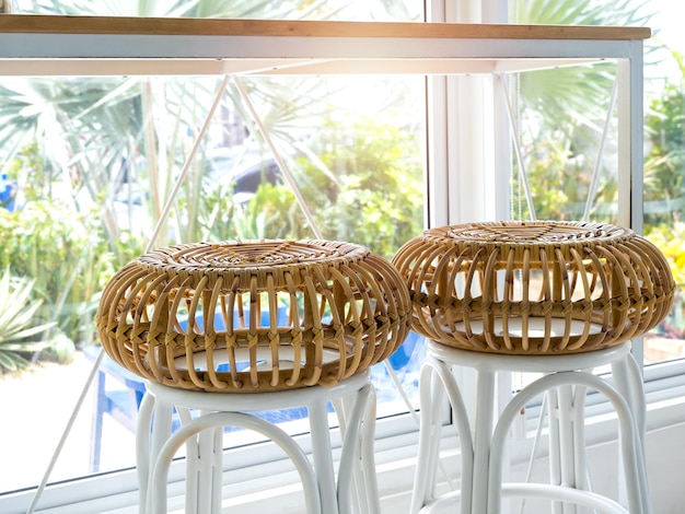 Duas cadeiras vazias de rattan bar perto da mesa e decoração de janela de vidro no café com vista para palmeira tropical verde do lado de fora
