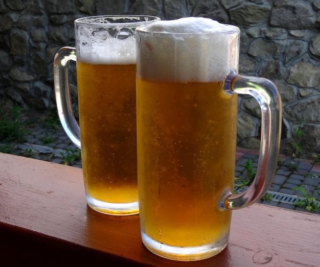 Duas canecas altas com cerveja gelada em uma grade de terraço na cervejaria com parede rochosa velha