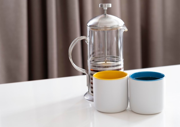 duas canecas brancas com azul e amarelo e um bule com carrinho de chá em uma mesa branca close-up