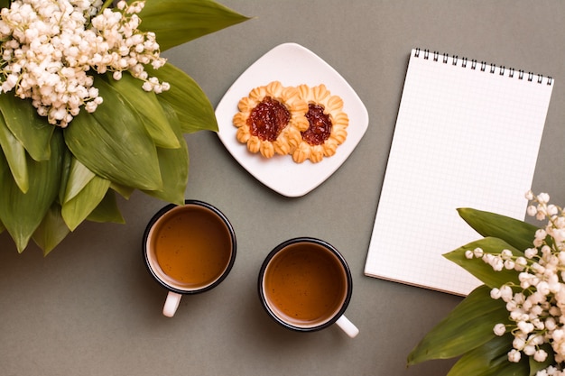 Duas canecas com chá, biscoitos, um caderno e buquês de lírios sobre uma mesa verde. pausa para descanso, vida lenta, planejamento, estabelecimento de metas. vista do topo