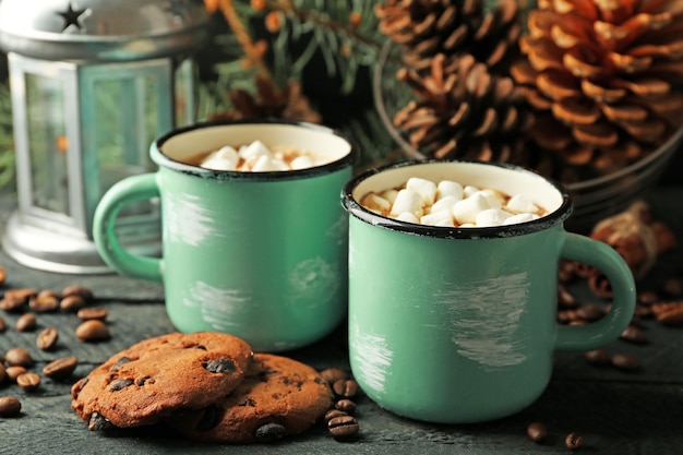 Duas canecas de cacau quente com marshmallow e biscoitos na mesa preta