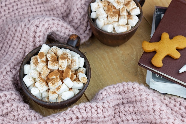 Duas canecas de chocolate quente com marshmallows ao lado de um suéter quente e um homem de gengibre