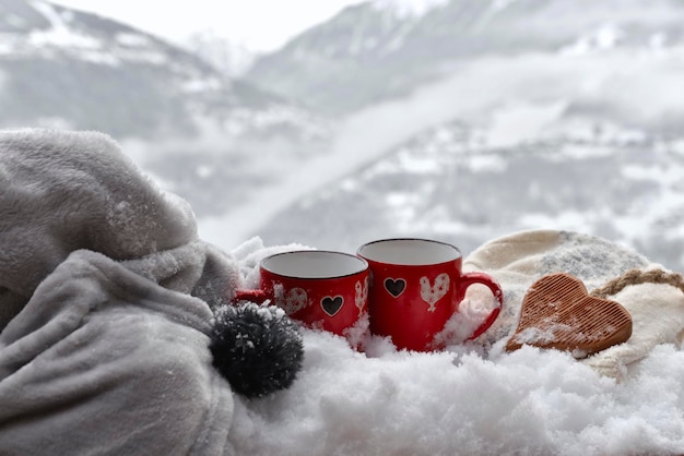 Duas canecas vermelhas com coração de madeira em forma de neve com cobertor na montanha