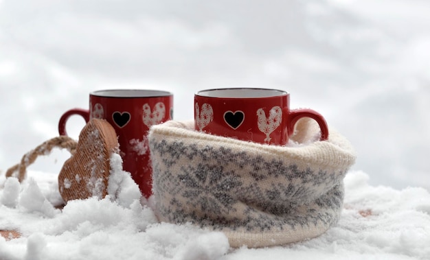 Duas canecas vermelhas com coração em forma de um chapéu de lã na neve