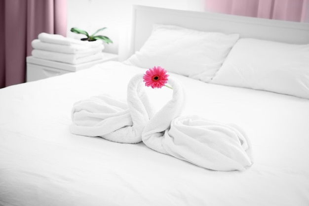 Duas cisnes de toalha e flores na cama no quarto de hotel