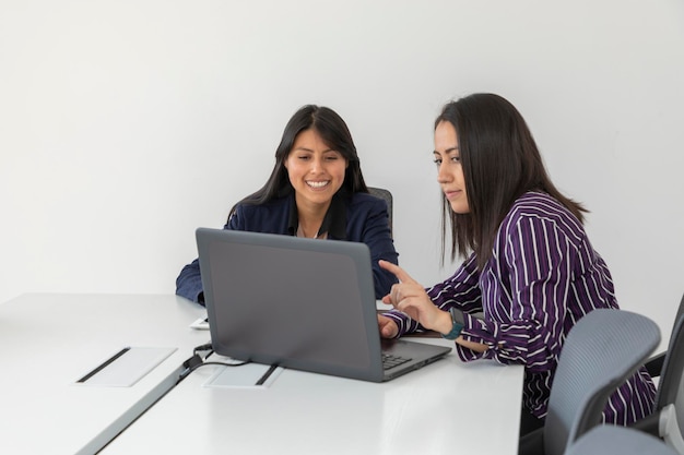 Duas colegas de trabalho conversam enquanto revisam um projeto em seu laptop Mulheres latinas trabalhando no escritório