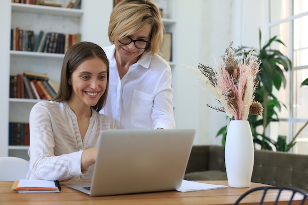 Duas colegas femininas trabalhando com laptop e discutindo um novo projeto.