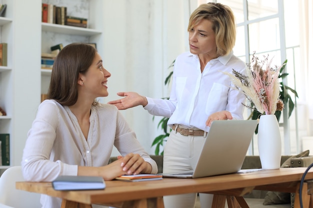 Duas colegas femininas trabalhando com laptop e discutindo um novo projeto.