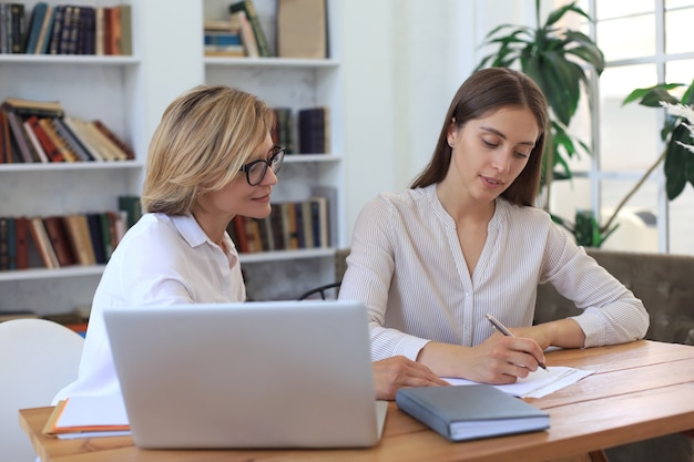 Duas colegas femininas trabalhando com laptop e discutindo um novo projeto.