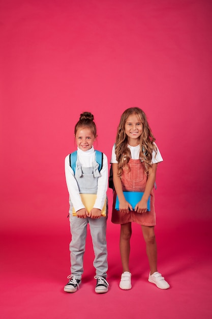 Foto duas colegiais alegres e felizes com mochilas e livros nas mãos. foto em um fundo rosa.