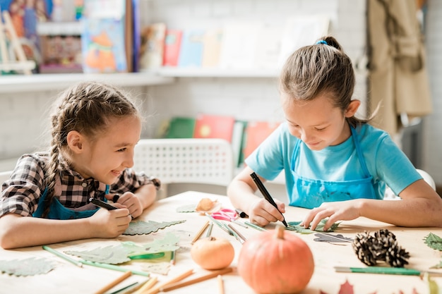 Duas colegiais alegres em trajes casuais sentadas à mesa enquanto trabalhavam na decoração de Natal na aula