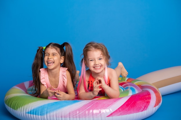 Duas criança feliz menina em fato de banho deitado no pirulito colorido colchão inflável na superfície azul.