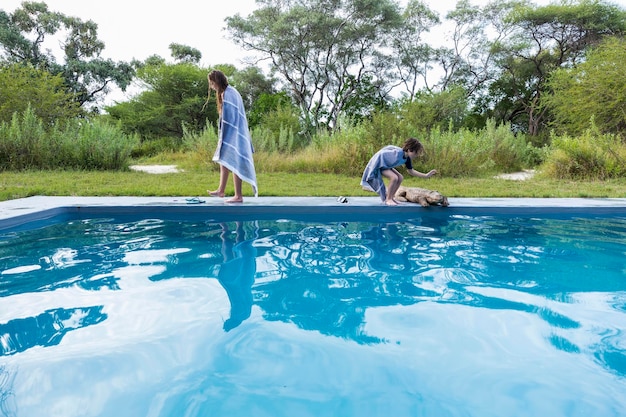 Duas crianças à beira de uma piscina, uma acariciando um grande crocodilo de madeira em um resort