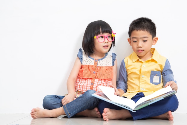 Duas crianças asiáticas lêem um livro no quarto de hóspedes.