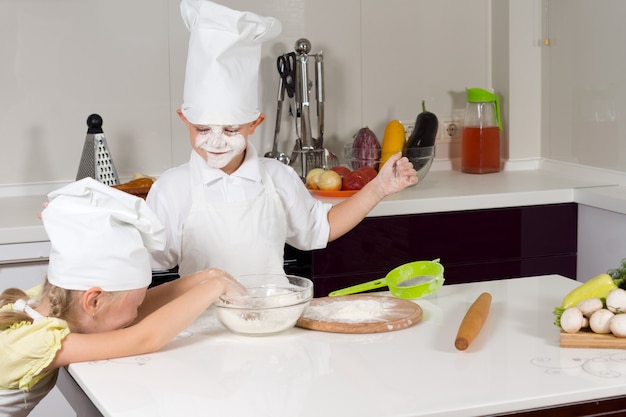Duas crianças bobas na cozinha brincando com farinha