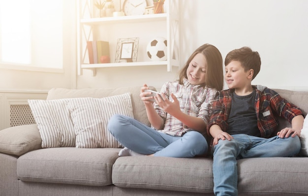 Duas crianças brincando no smartphone enquanto está sentado no sofá em casa.