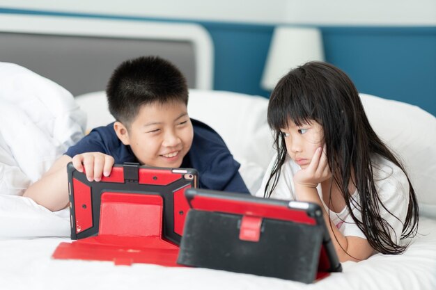 Duas crianças chinesas viciadas em tablet criança asiática assistindo telefone juntos em sua cama usando smartphone