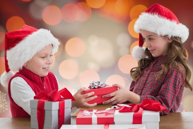 Duas crianças com chapéu de papai noel compartilhando caixas de presente de natal
