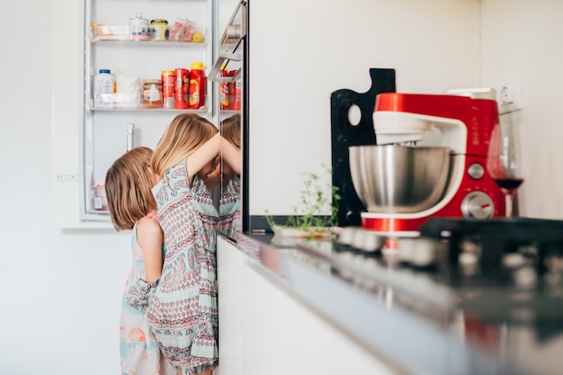 Duas crianças com fome do sexo feminino irresistivelmente com fome procurando comida na geladeira