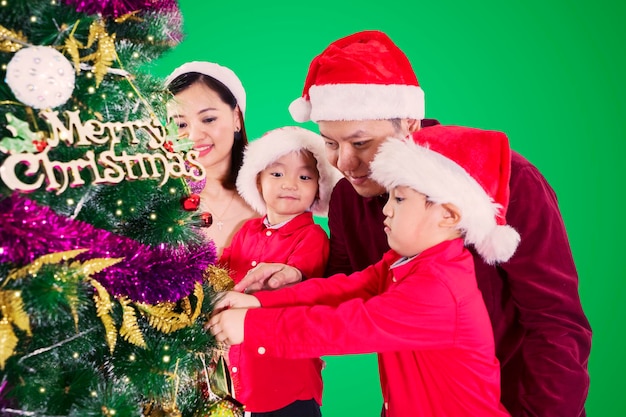 Duas crianças e seus pais preparando uma árvore de Natal juntos em casa