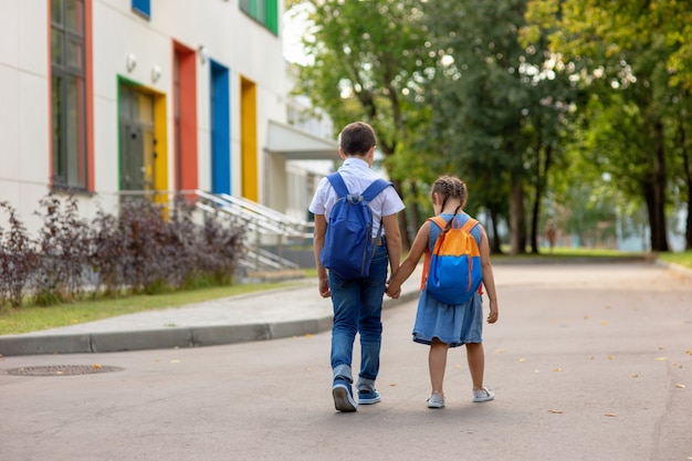 Duas crianças em idade escolar, uma menina e um menino de mochila nas costas, vão a caminho da escola