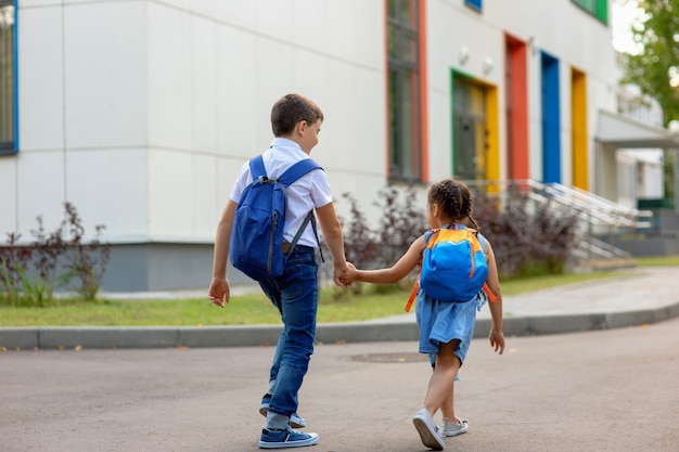 Duas crianças em idade escolar, uma menina e um menino em uma camisa branca com mochilas vão a caminho da escola