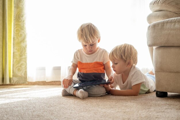 Duas crianças engraçadas gêmeos meninos usando tablet assistindo desenhos no chão em casa