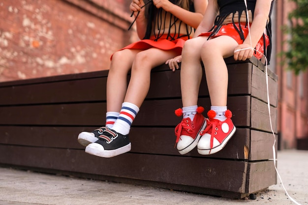 Duas crianças estão sentadas descansando em um banco da cidade Os sapatos esportivos infantis são vermelhos e pretos com cadarços