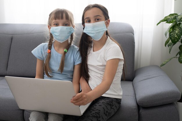 Duas crianças felizes aprendendo, estudando on-line e trabalhando no laptop com máscara facial.