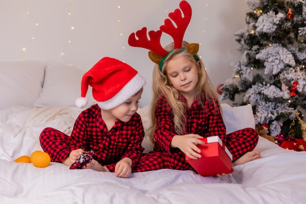 duas crianças felizes de pijama para o Natal estão classificando presentes e brincando com brinquedos de Natal