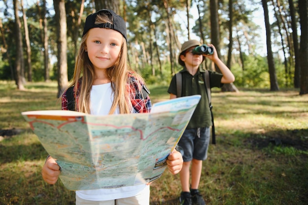 Duas crianças felizes se divertindo durante a caminhada na floresta em lindo dia na floresta de pinheiros Escoteiro bonito com binóculos durante caminhadas na floresta de verão Conceitos de escotismo de aventura e turismo de caminhadas