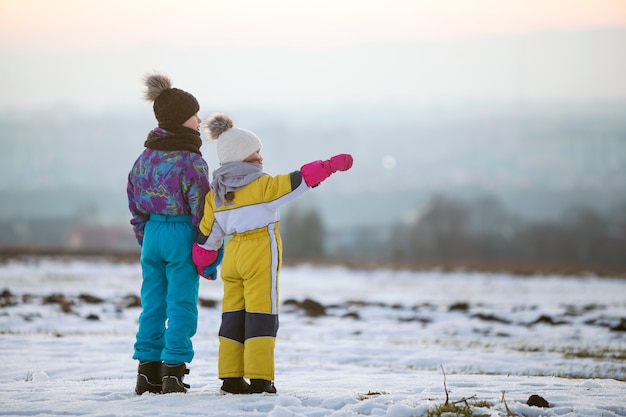 Duas crianças irmão e irmã que estão fora no campo coberto de neve do inverno que guarda as mãos.