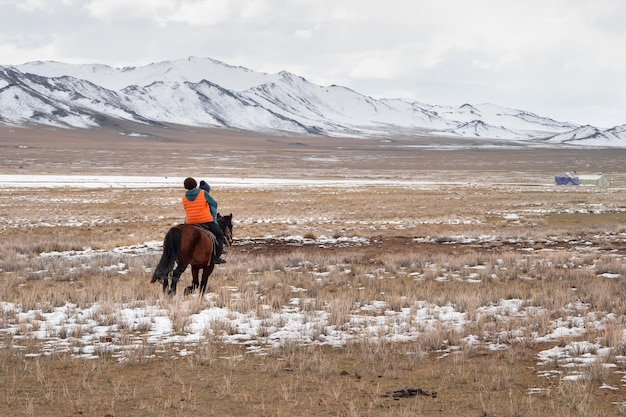 Duas crianças montando um cavalo vista de trás uma iurta em um planalto nevado vida nômade na Mongólia uma ampla extensão