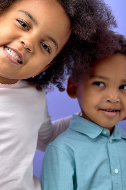 Foto duas crianças negras animadas posando para a câmera e sorrindo alegremente sobre roxo