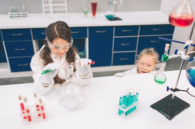 Duas crianças no jaleco aprendendo química no laboratório da escola. Jovens cientistas em óculos de proteção fazendo experimento em laboratório ou gabinete de químico. Estudando ingredientes para experimentos.