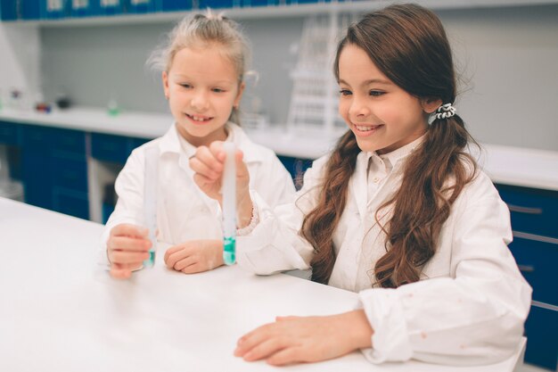 Duas crianças no jaleco aprendendo química no laboratório da escola. jovens cientistas em óculos de proteção fazendo experimento em laboratório ou gabinete de químico. estudando ingredientes para experimentos.