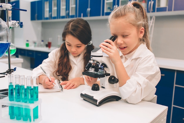 Duas crianças no jaleco aprendendo química no laboratório da escola. jovens cientistas em óculos de proteção fazendo experimento em laboratório ou gabinete de químico. olhando através do microscópio