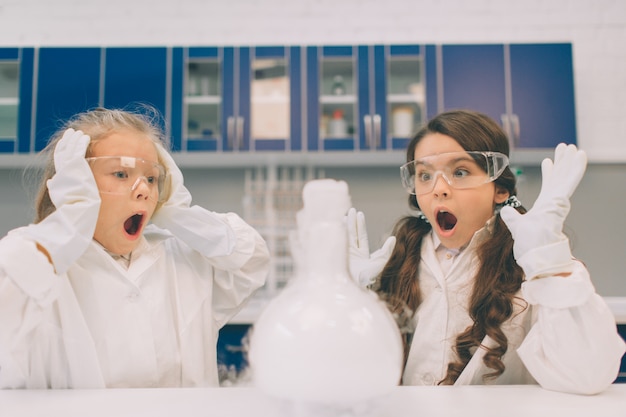 Duas crianças no jaleco aprendendo química no laboratório da escola. jovens cientistas em óculos de proteção fazendo experimento em laboratório ou gabinete químico. experiências perigosas.