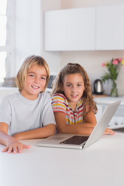 Duas crianças olhando a câmera com laptop na frente