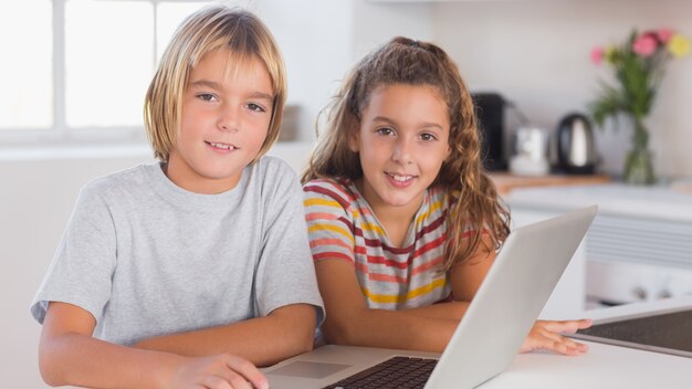 Duas crianças olhando a câmera junto com laptop na frente