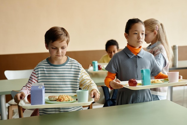 Duas crianças segurando bandejas de almoço na mesa na cafeteria da escola