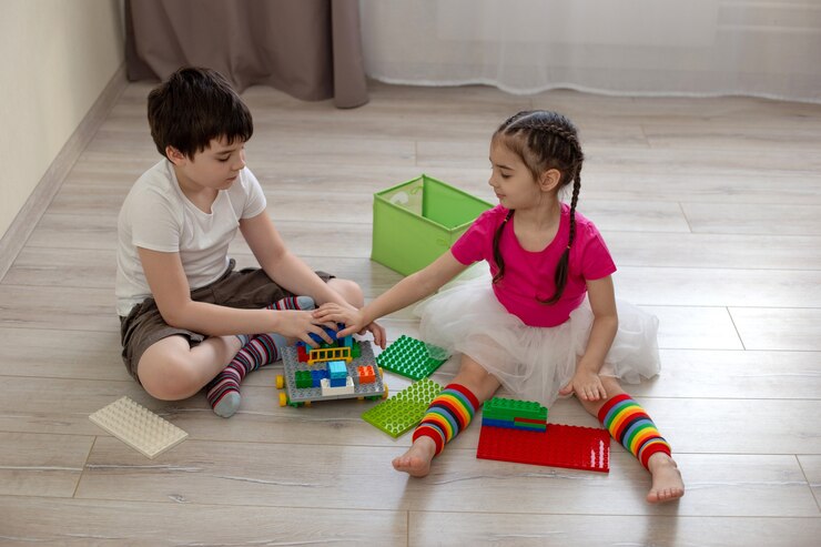 Foto duas crianças, um menino e uma menina, sentam-se no chão e brincam em construções de plástico