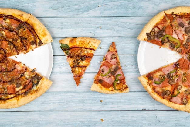 Foto duas deliciosas pizzas grandes diferentes em um fundo azul de madeira.