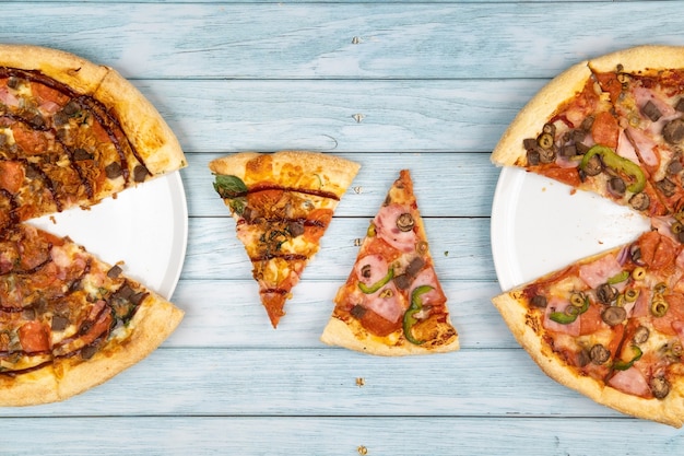 Duas deliciosas pizzas grandes diferentes em um fundo azul de madeira.
