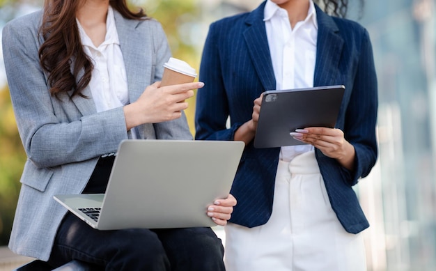 Duas empresárias asiáticas discutem a estratégia de trabalho e planejamento de projetos de investimento com o laptop tablet no escritório externo