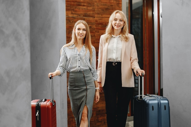 Duas empresárias caucasianas entrando no hotel com malas prontas