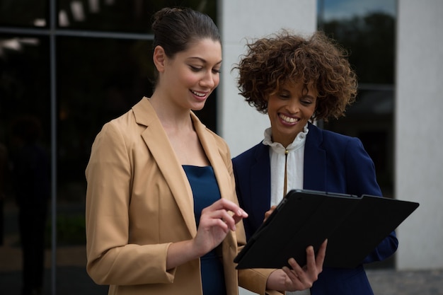 Duas empresárias usando tablet digital perto de prédio comercial