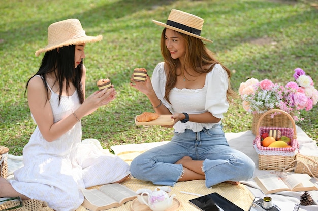 Duas encantadoras jovens asiáticas compartilhando seus doces e fazendo piquenique juntas no jardim