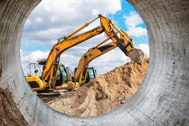 Duas escavadeiras poderosas trabalham ao mesmo tempo em um céu azul ensolarado do canteiro de obras ao fundo Equipamento de construção para terraplanagem