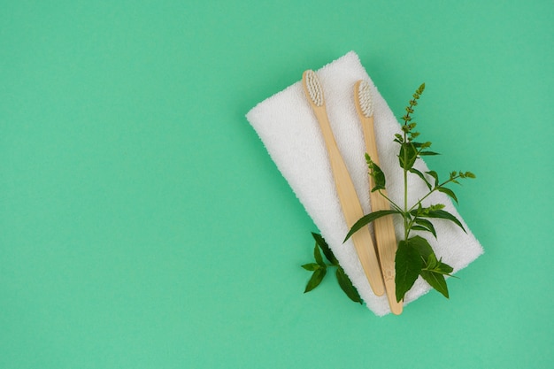 Duas escovas de dente feitas de material ecológico com um raminho de hortelã verde e uma toalha branca em um fundo de hortelã